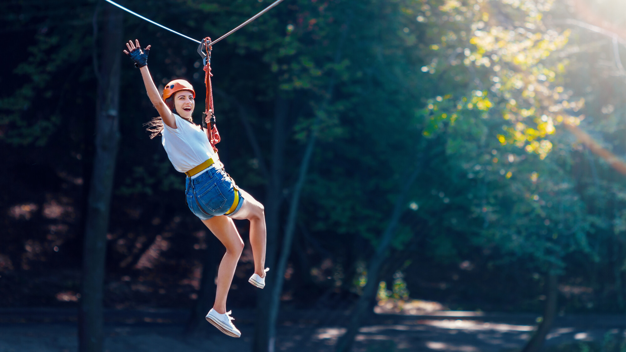 Eine Frau fährt lachend und winkend eine Zipline entlang.