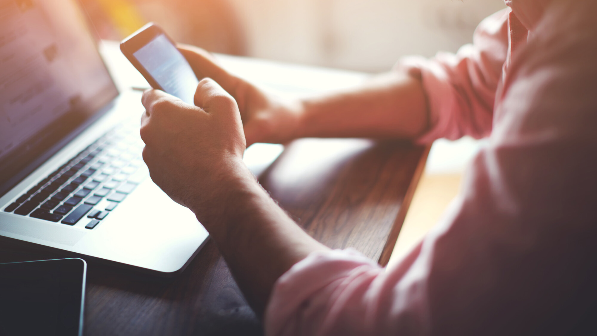Seitenansicht der Hände eines Mannes, der sein Smartphone benutzt an seinem Arbeitsplatz.