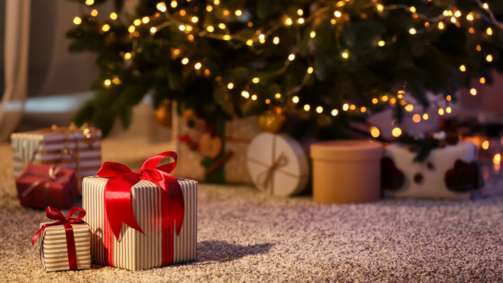 Geschenke auf dem Teppich vor einem Weihnachtsbaum mit Lichterkette