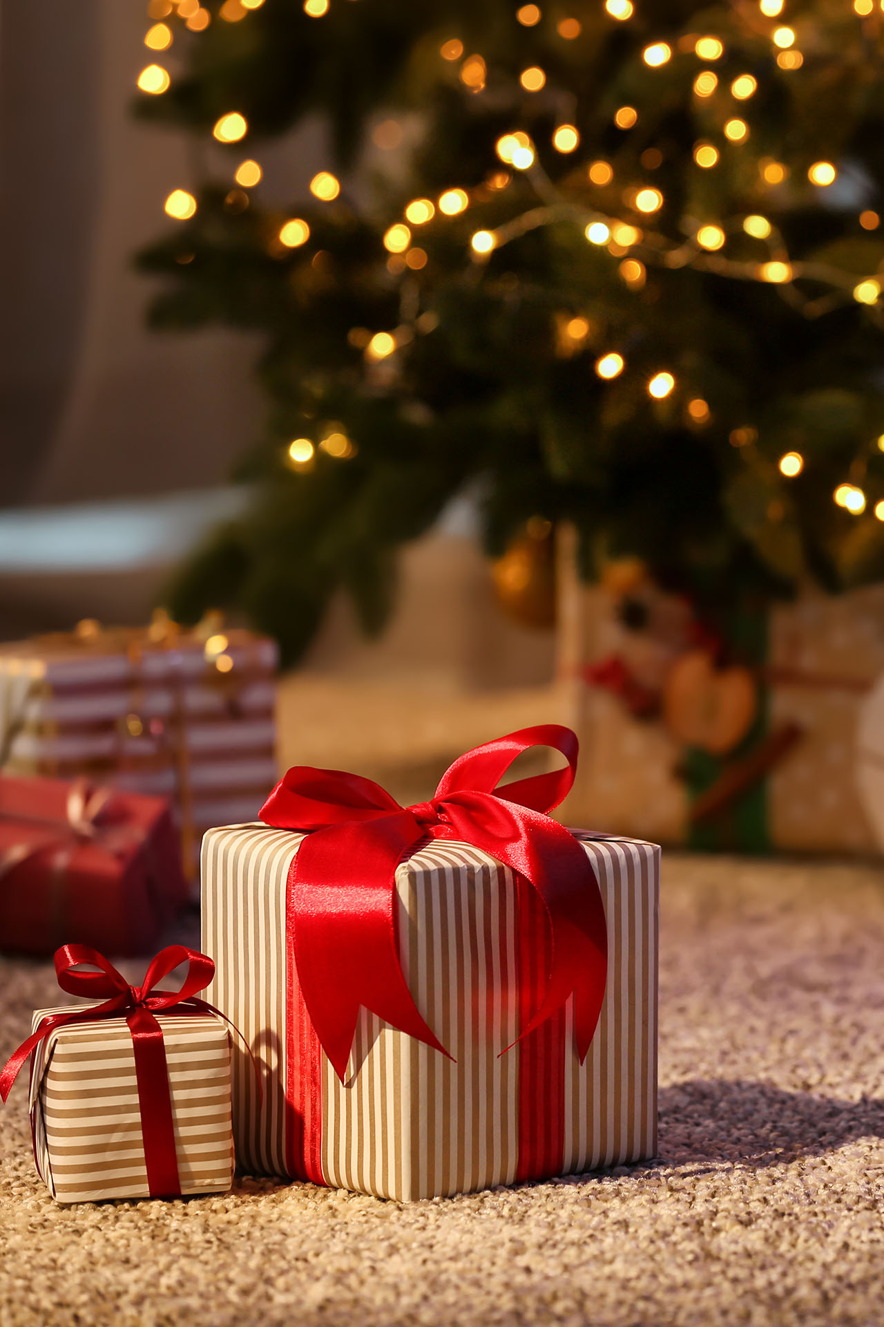 Geschenke auf dem Teppich vor einem Weihnachtsbaum mit Lichterkette
