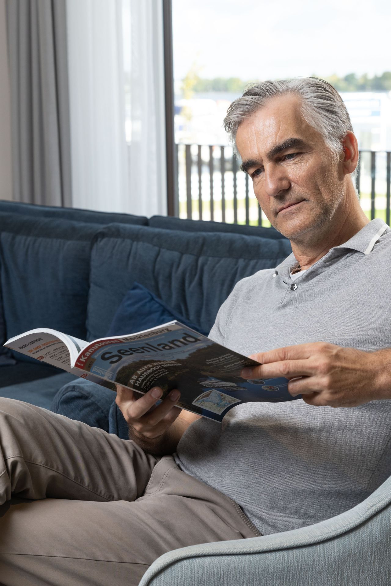 Mann liest Zeitschrift auf einem Sofa.