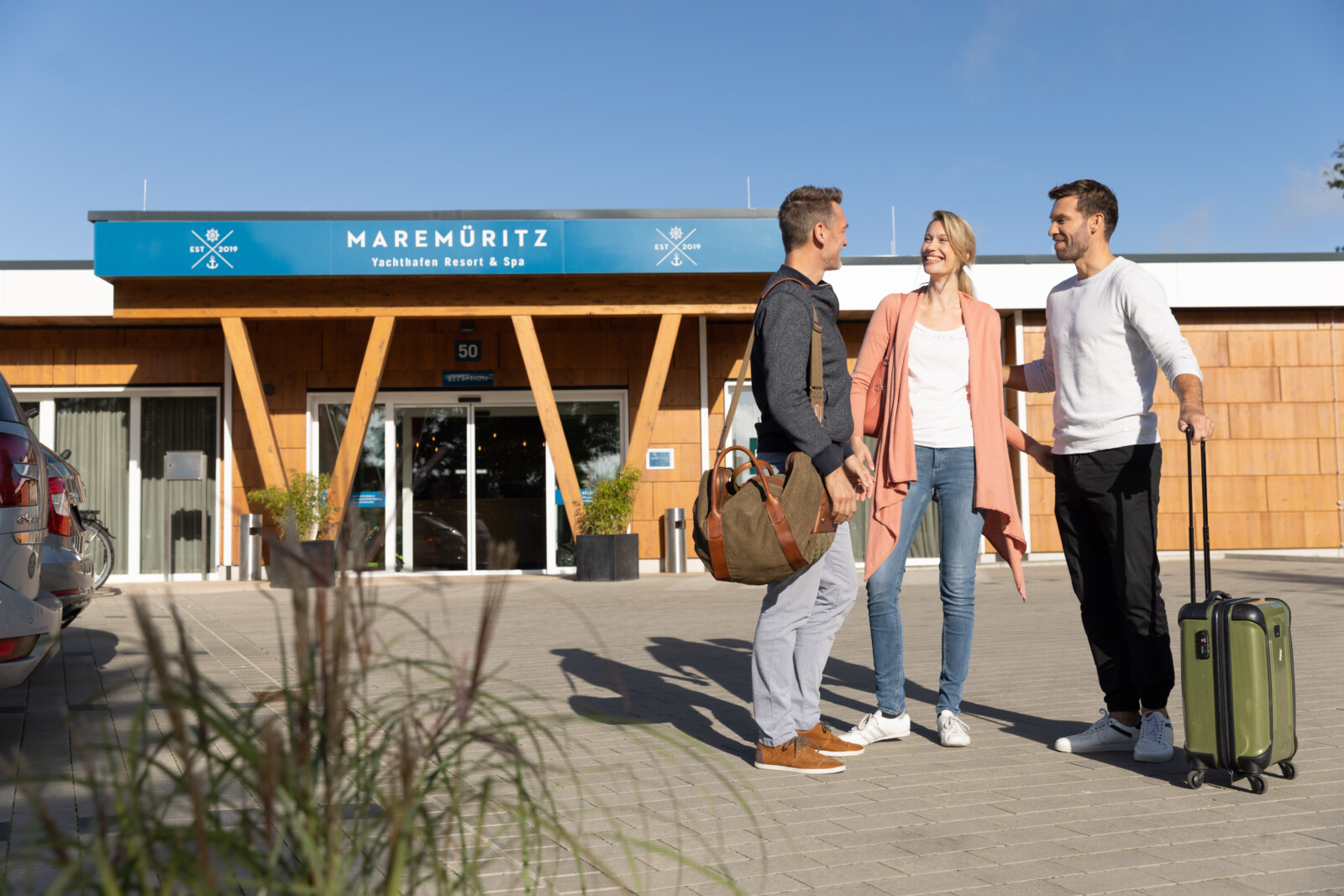 Drei Menschen mit Gepäck kommen im MareMüritz Yachthafen Resort an.