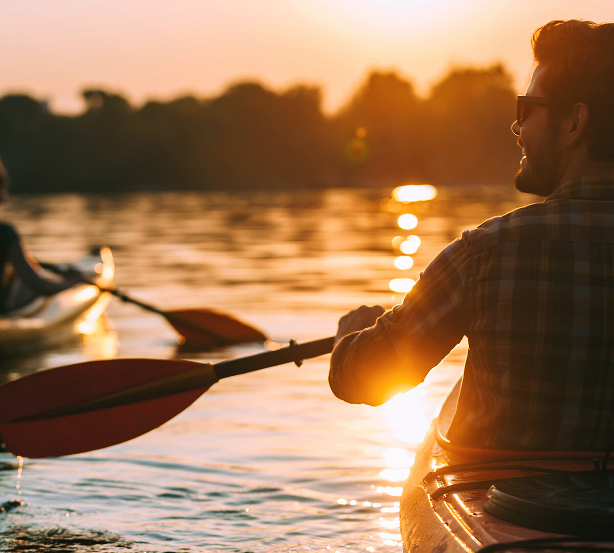 Ein Mann und eine Frau fahren Kajak auf dem Wasser im Sonnenuntergang.