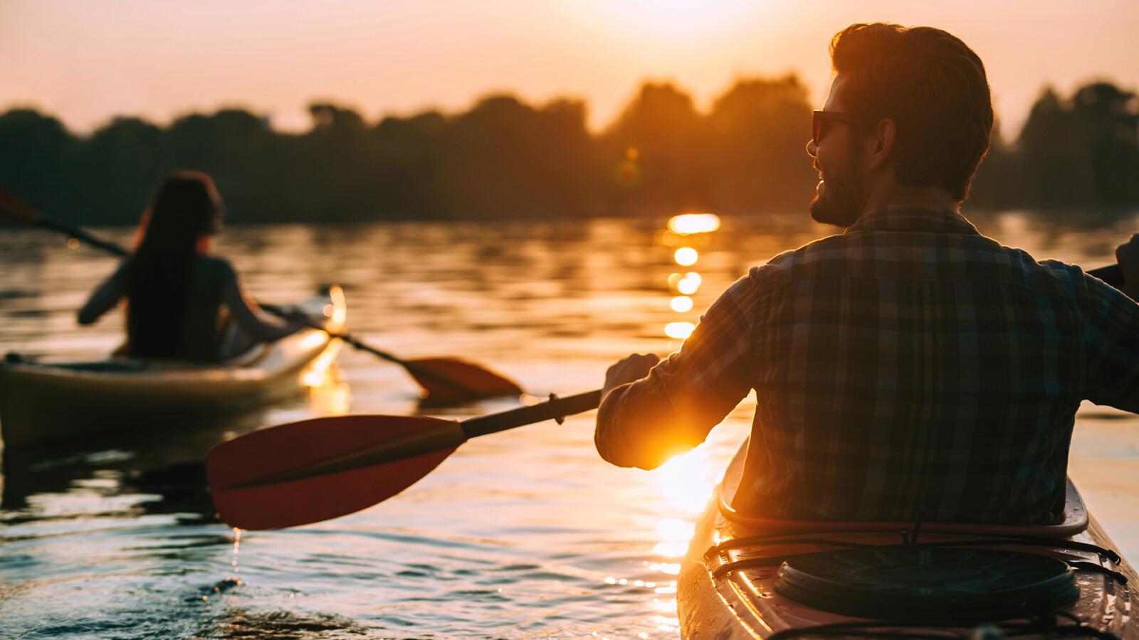 Ein Mann und eine Frau fahren Kajak auf dem Wasser im Sonnenuntergang.