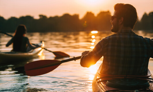 Ein Mann und eine Frau fahren Kajak auf dem Wasser im Sonnenuntergang.