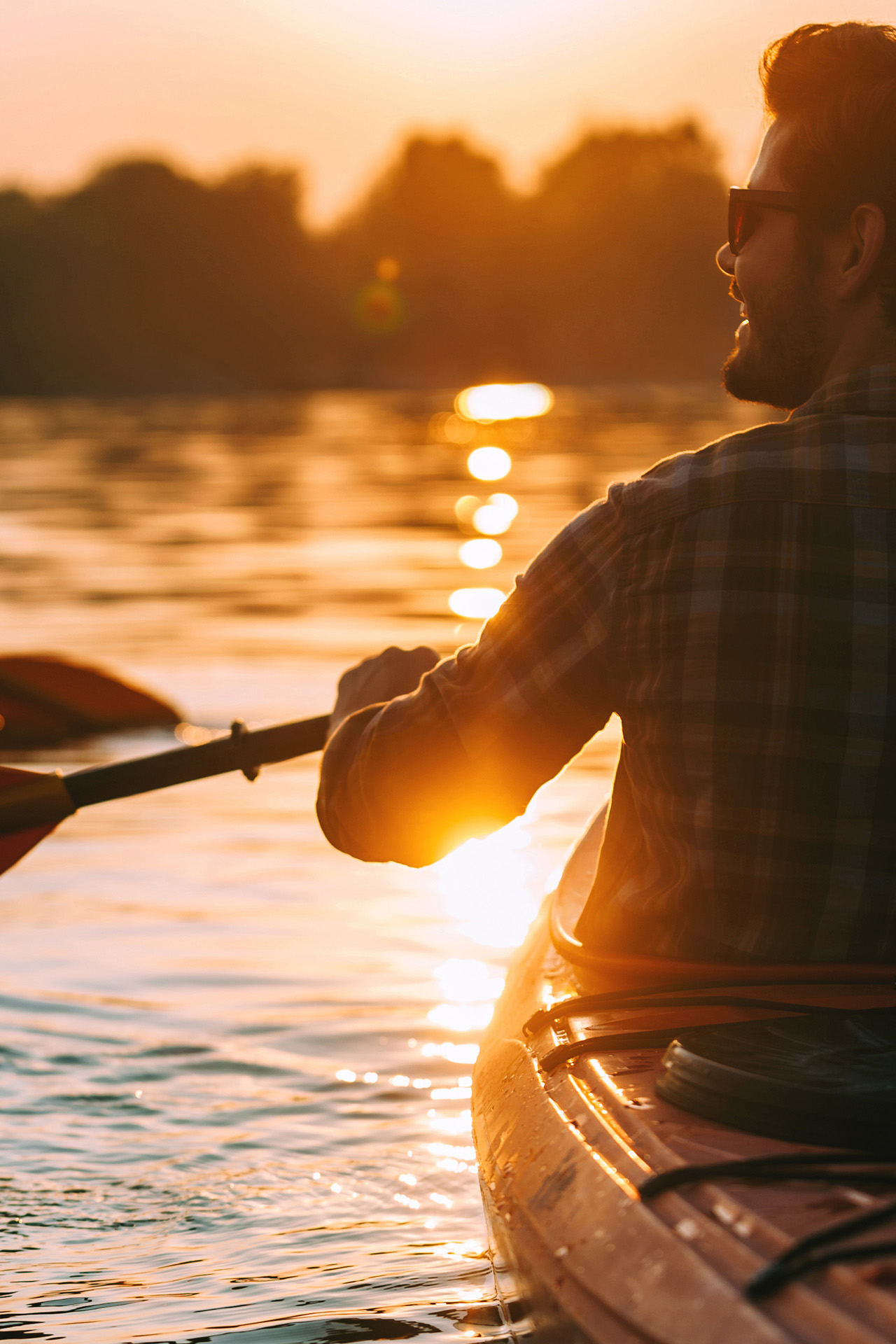 Ein Mann fährt Kajak auf dem Wasser im Sonnenuntergang.