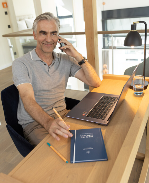 Mann beim Telefonieren vor einem Laptop am Schreibtisch im Apartment.