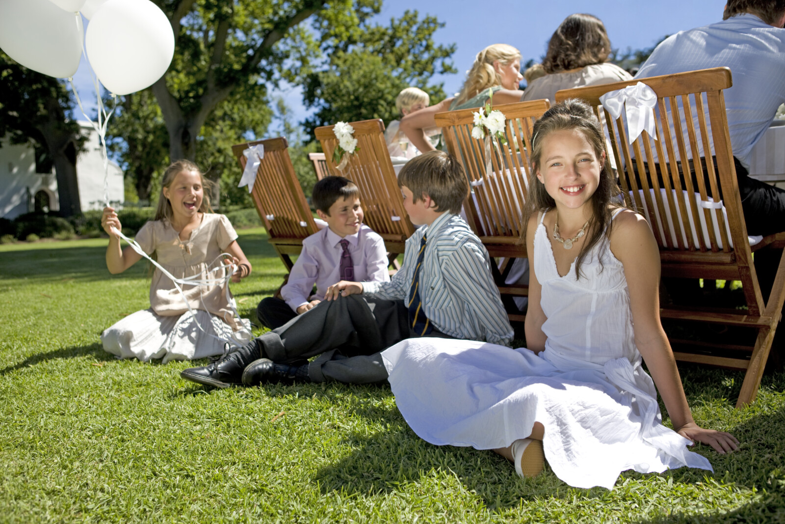 Eine Gruppe von der Kindern sitzt bei einer Hochzeit auf einer Wiese.
