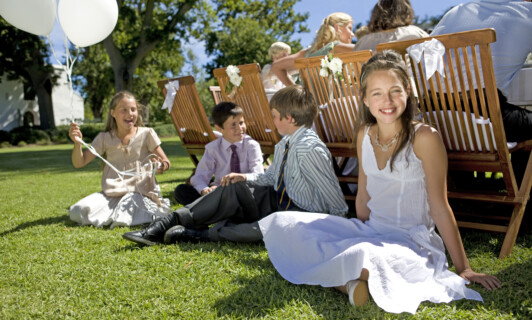 Eine Gruppe von der Kindern sitzt bei einer Hochzeit auf einer Wiese.