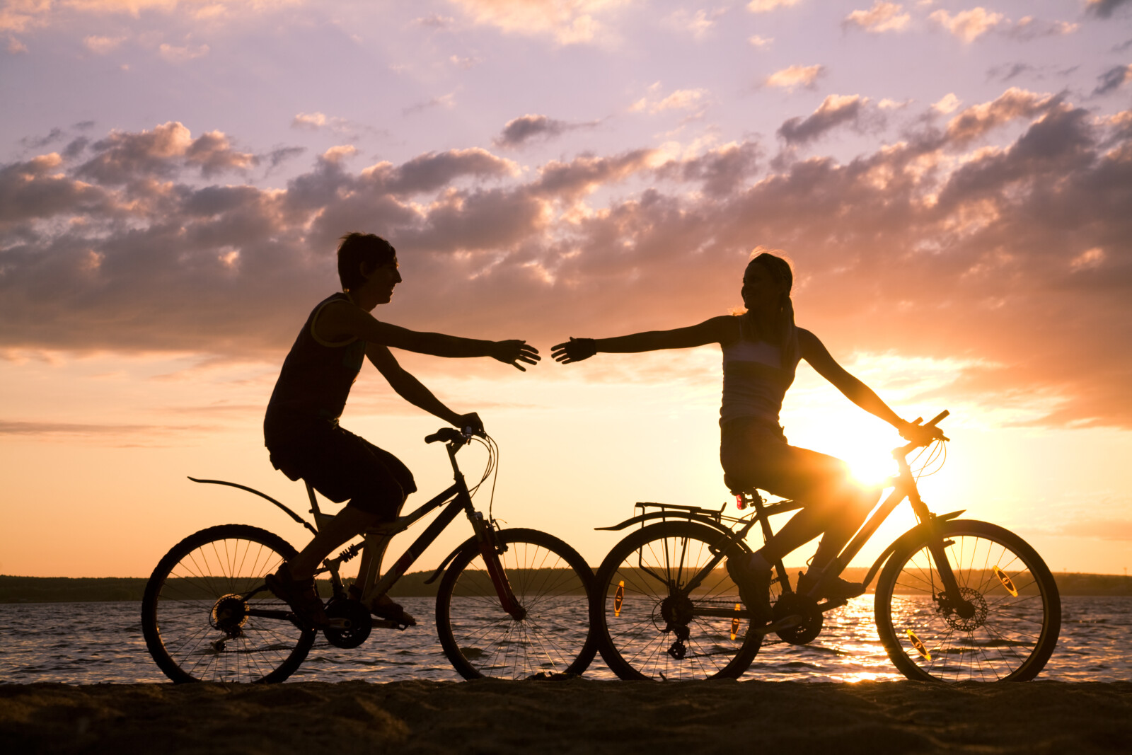 Glückliches Paar fährt Fahrrad und streckt sich die Hände entgegen.