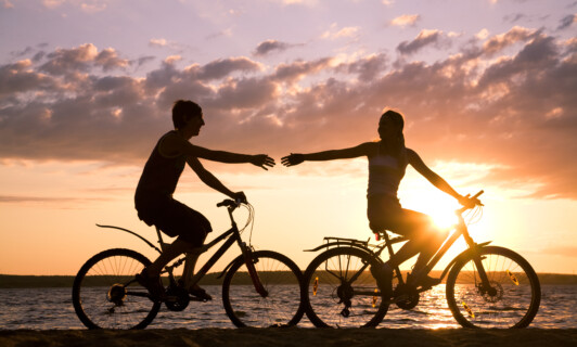 Glückliches Paar fährt Fahrrad und streckt sich die Hände entgegen.