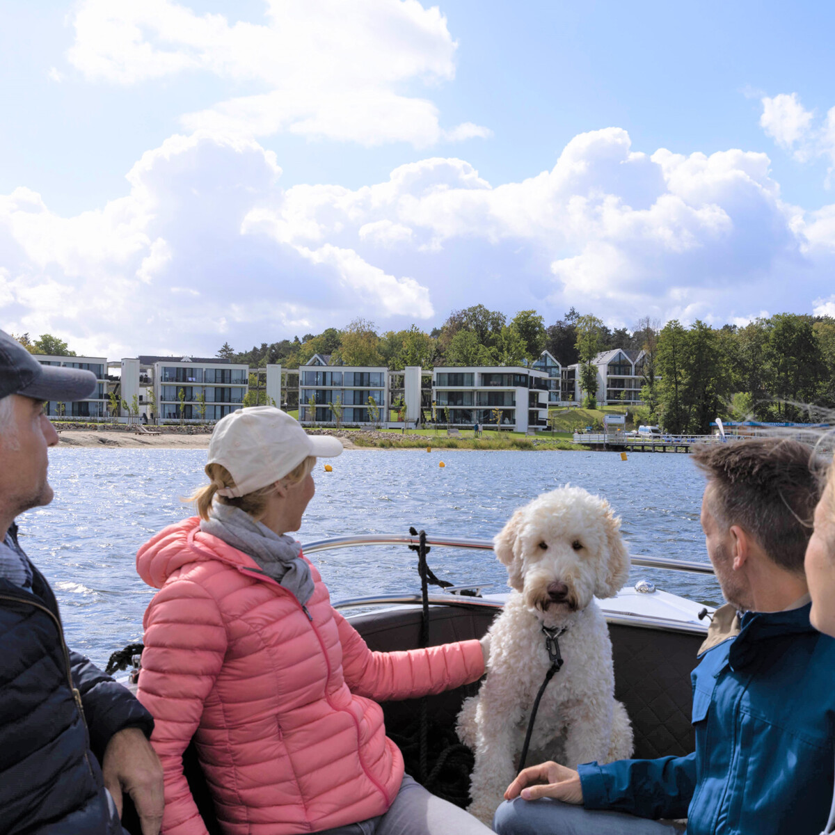 Gruppe von Menschen und ein Hund auf einem Boot mit Blick auf das MareMüritz Yachthafen Resort.