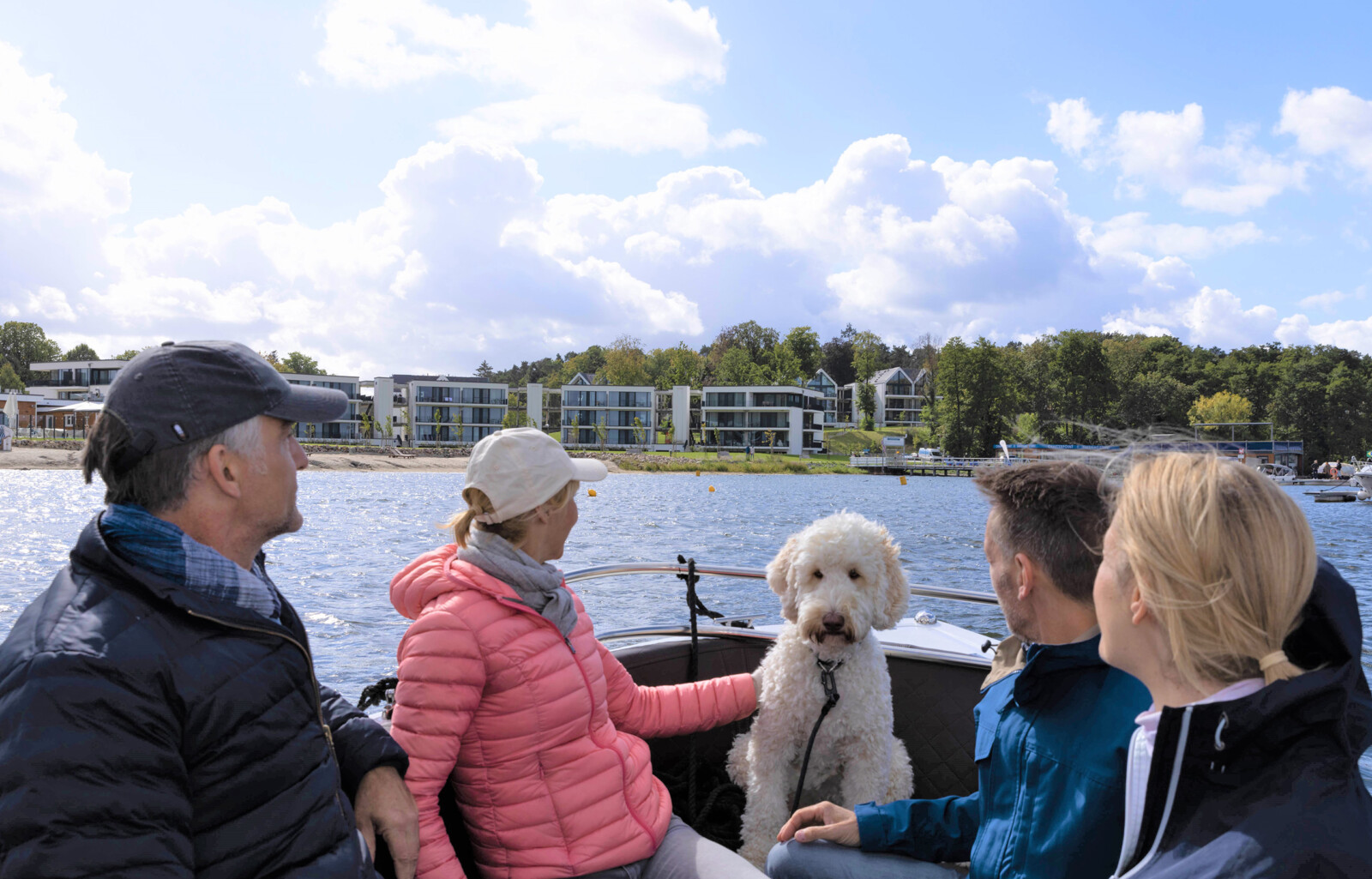 Gruppe von Menschen und ein Hund auf einem Boot mit Blick auf das MareMüritz Yachthafen Resort.