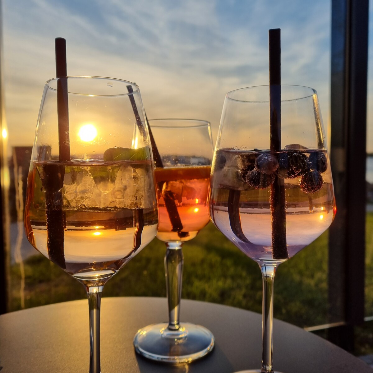 Drei Cocktails im Sonnenuntergang auf einem Tisch.