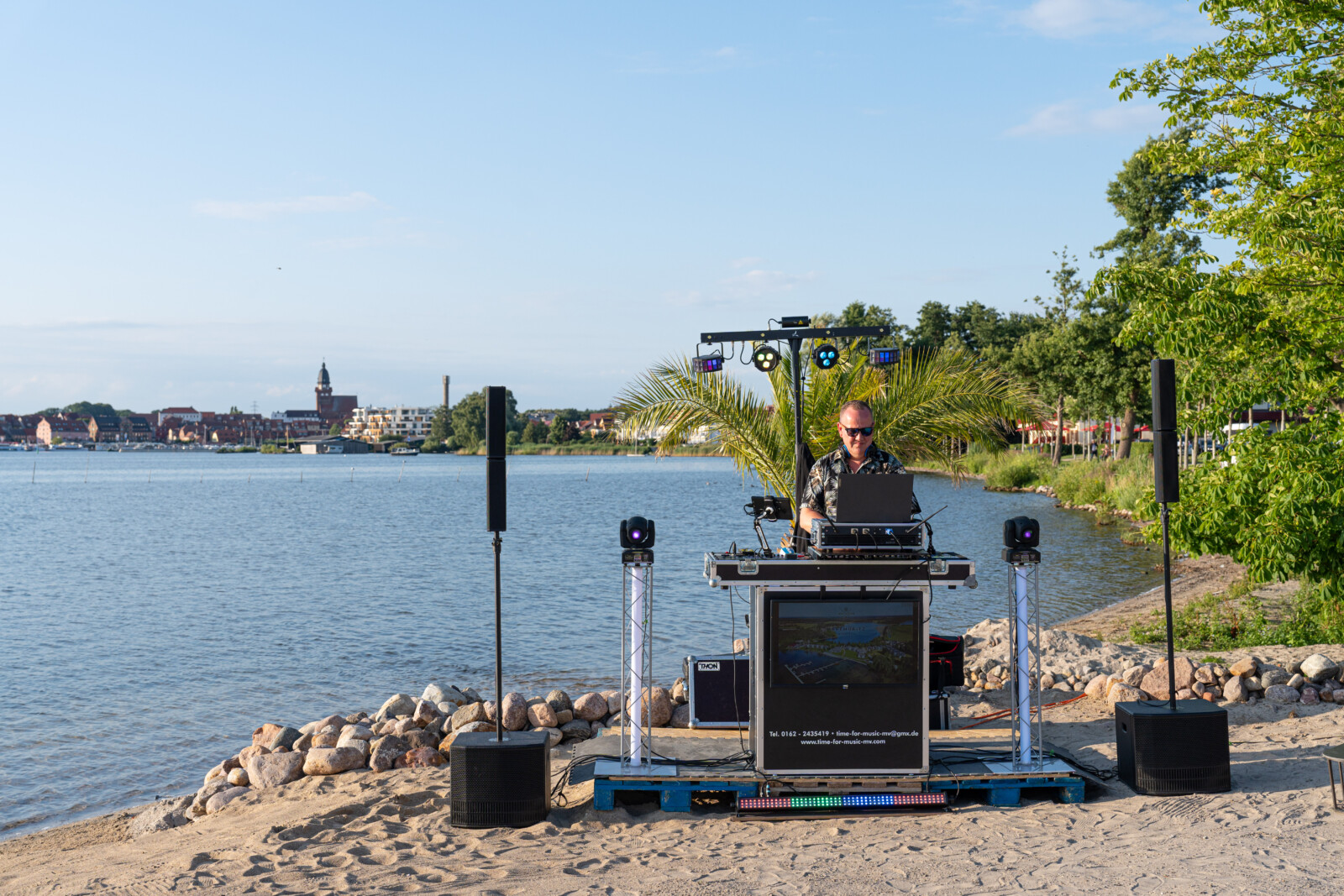 DJ am Strand an der Müritz mit Waren Müritz im Hintergrund.