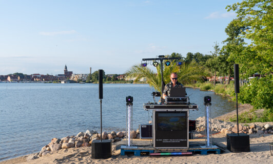 DJ am Strand an der Müritz mit Waren Müritz im Hintergrund.