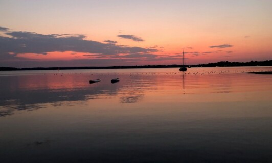 Sonnenuntergang mit Segelboot über einem See.