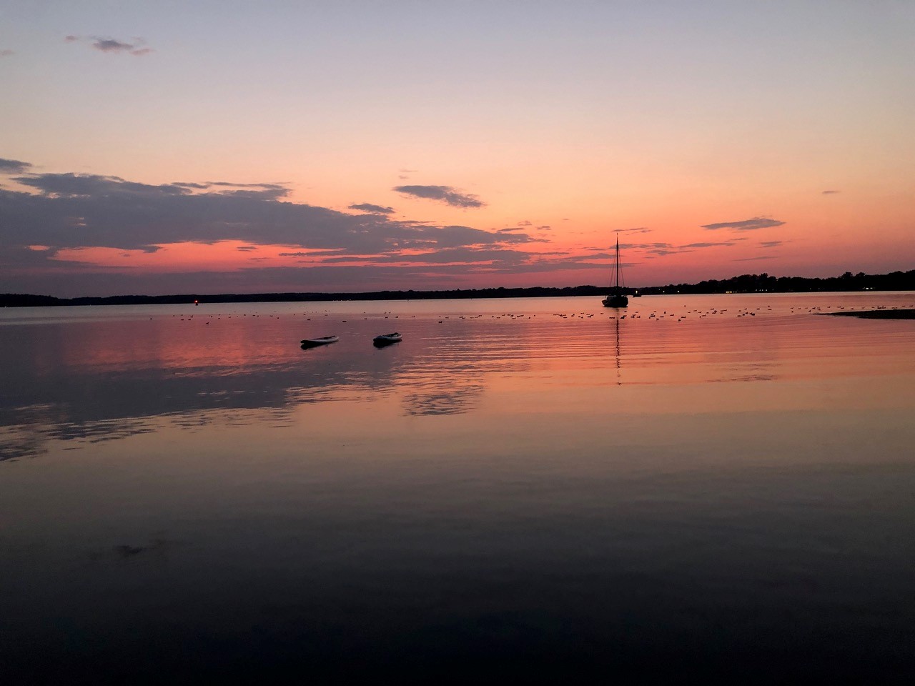 Sonnenuntergang mit Segelboot über einem See.