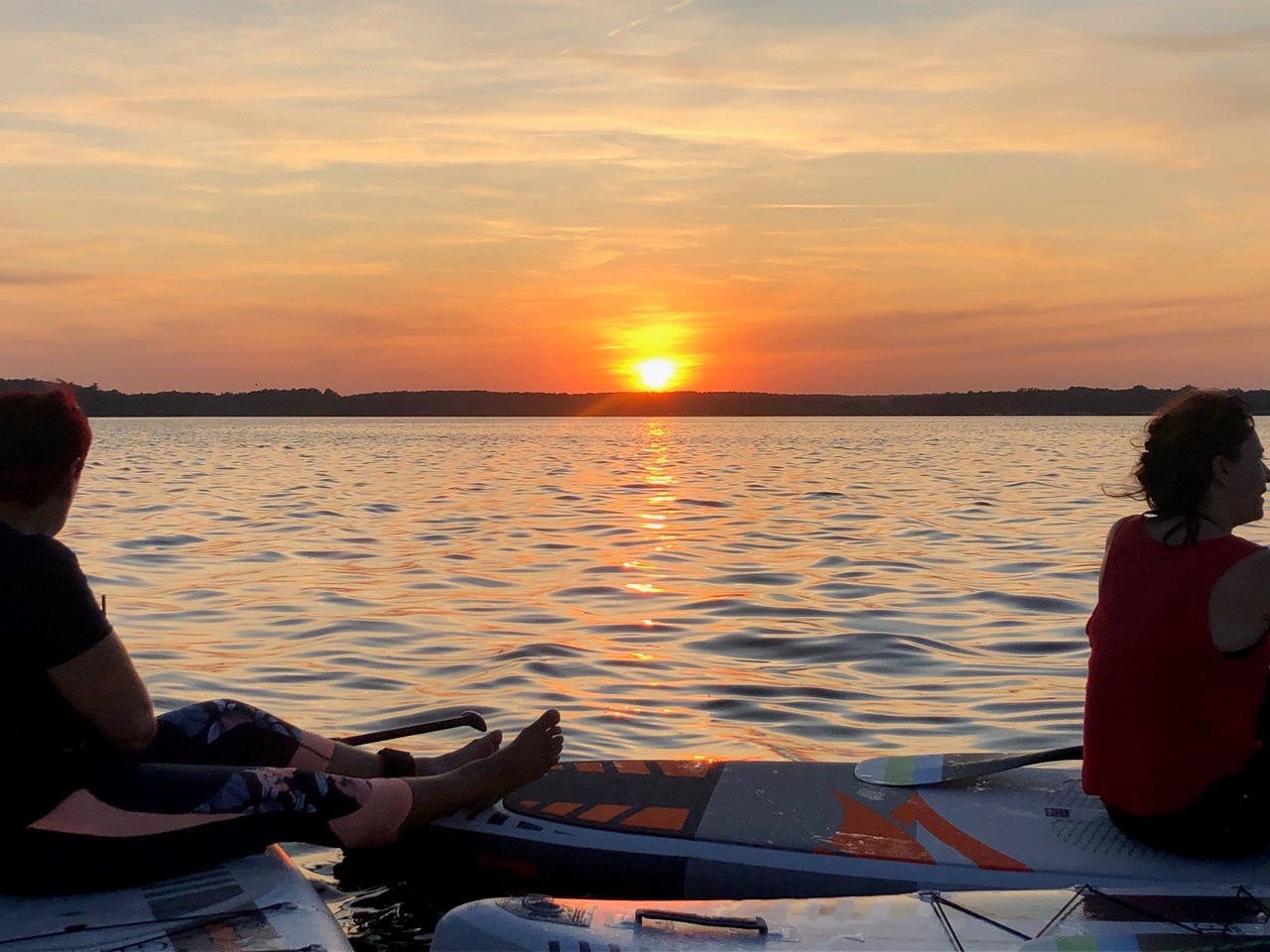 Frauen sitzen auf Stand-Up-Paddle-Boards und beobachten einen Sonnenuntergang.