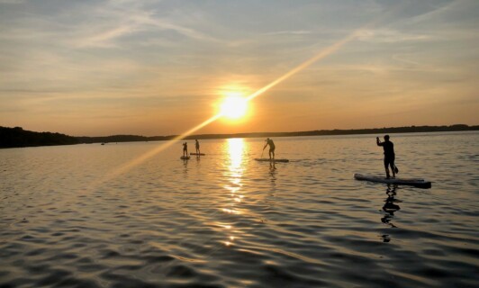 Eine Gruppe beim Stand-Up Paddeling auf der Müritz beim Sonnenuntergang.