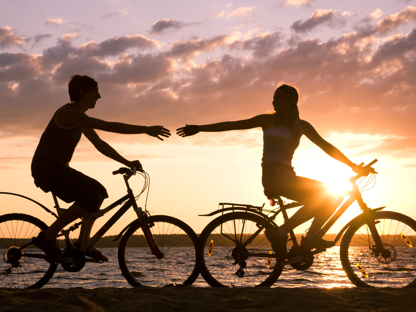 Ein Pärchen fährt am Seeufer vor einem Sonnenuntergang gemeinsam Fahrrad.