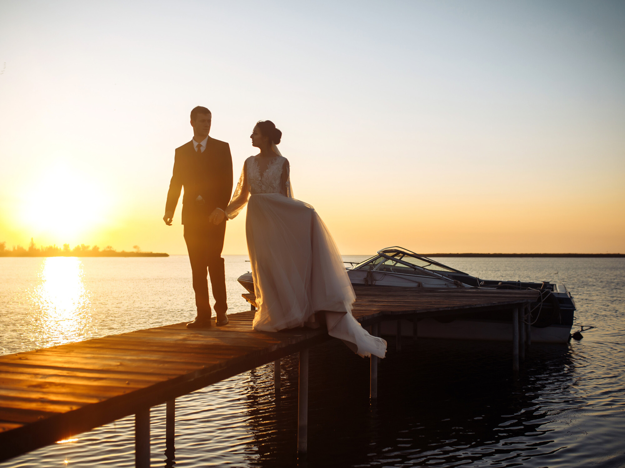 Hochzeitspaar auf einem Steg vor einem Boot im Sonnenuntergang im Yachthafen Resort Maremüritz.