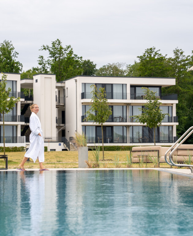 Frau spaziert im Bademantel entlang des Außenpools des Aparthotels Maremüritz in Waren